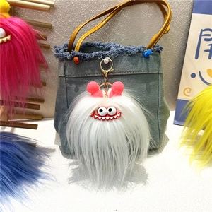 Detail of white fluffy monster plush keychain with pink ears on a blue denim bag