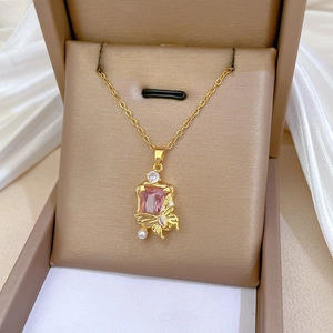 Macro view of gold butterfly pendant with pink crystal and pearl detail on silk