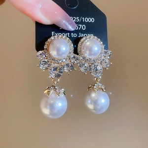 Macro view of crystal flower earrings with large white pearl drop on black card