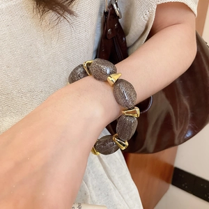 Detail of acrylic oval beaded bracelet with gold accents worn by a model in casual style
