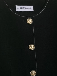 Detail of black blazer neckline with white contrast stitching and gold spiral buttons