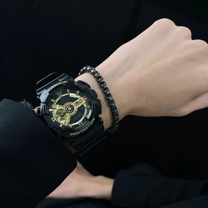 Close-up of black and gold sports watch and woven bracelet on wrist with dark background