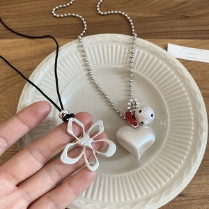 Close-up of floral and heart pendants with silver ball chain and black cord necklace
