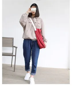 Detail of a casual large red canvas crossbody bag paired with a beige hoodie and jeans