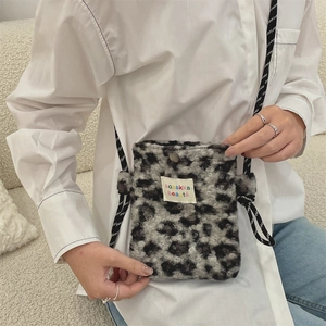Detail of leopard print plush crossbody bag with woven strap and logo patch on soft fabric