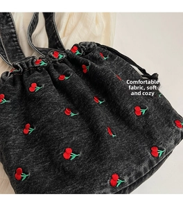 Close-up of black denim bucket bag with red cherry embroidery and drawstring details