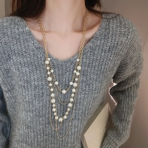 Detail of layered faux pearl necklace on a gray sweater showing golden chain texture