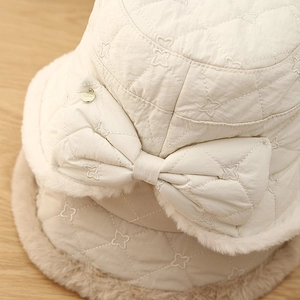Detailed macro view of quilted cream bucket hat with plush faux fur trim and bow