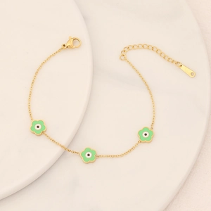 Detail of gold flower bracelet with green petals and evil eye charms on ceramic plate