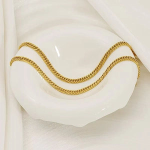 Elegante goldene Edelstahl Schlangenkette auf weißer Keramikschale vor Seidenhintergrund