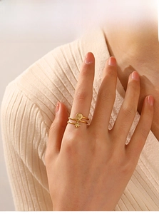 Detail of gold layered starburst and disc ring worn on finger with soft knit sweater