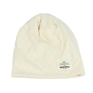 Close-up of cream knit beanie featuring geometric diamond texture and woven label