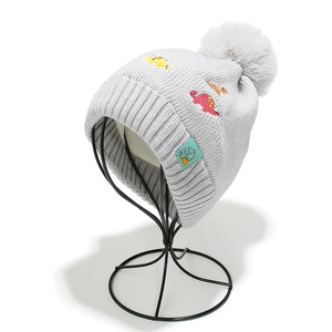 Detail of grey knitted kids hat featuring colorful dinosaur embroidery and soft pompom