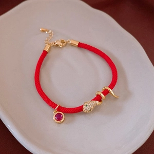 Détail du bracelet tressé rouge avec breloque serpent dorée et pierre précieuse rouge