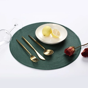 Close-up of green round woven placemat with gold cutlery set and white plate setting