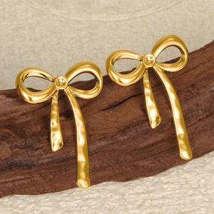 Detailed view of matte gold bow earrings with hanging ribbons on rustic wood background
