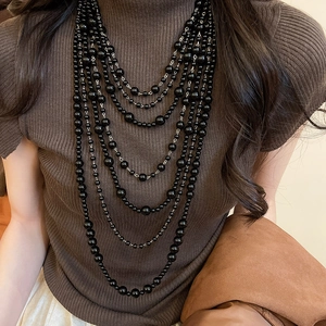 Detailed close-up of multi-layer black acrylic beaded necklace on knitwear sweater