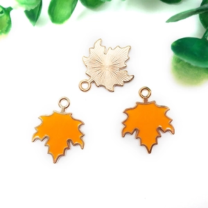 Detailed macro view of three orange enamel maple leaf metal pendants for DIY jewelry