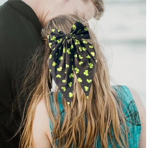 Elegant black bow hair clip with vibrant green clover print on blonde ponytail