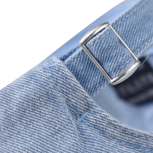 Detail of adjustable metal buckle and stitching on washed light blue denim baseball cap