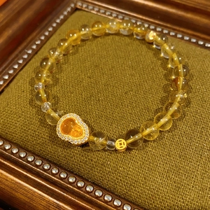 Detail of yellow citrine beaded bracelet with gold gourd and coin charms on green pad