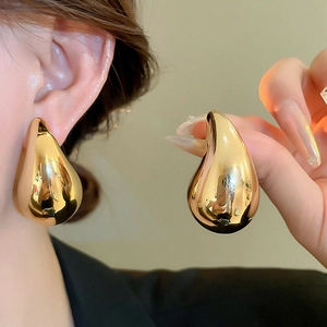 Macro shot of large polished gold water drop earrings in a luxurious minimalist style