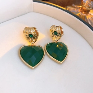 Close-up of golden earrings with faceted green heart gemstones in a jewelry box