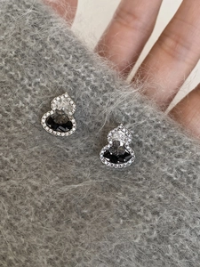 Close-up of silver-tone gourd earrings with black zircon stones on gray knit background