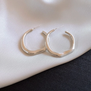 Macro detail of silver irregular streamline hoop earrings on silk and textured fabric