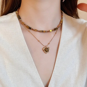 Close-up of double-layered gold necklace with beaded chain and heart-shaped gemstone pendant