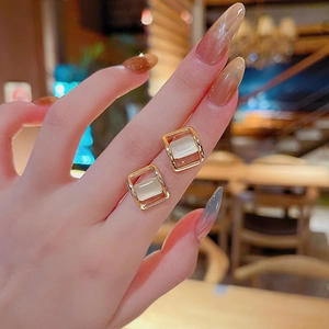 Close-up of gold square stud earring with opal stone worn on ear in warm setting