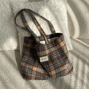 Detail of vintage plaid wool tote bag showing thick texture and fabric label on a soft rug