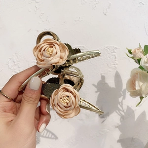 Detail of elegant gold metal hair claw with beige fabric roses and green leaves