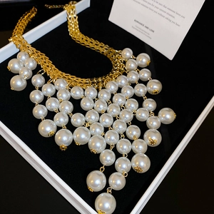Detail of elegant gold fringe necklace with layered faux pearls on black velvet display