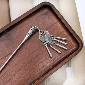 Close-up of vintage silver tassel hairpin with fan-shaped pendant on a dark wooden tray