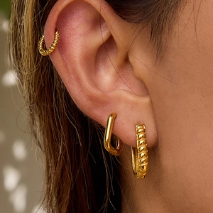 Close-up of golden twisted hoop earrings and rectangular studs worn by a model