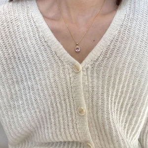 Close-up of gold necklace featuring pink oval gemstone pendant on a white sweater