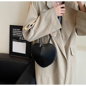 Dettaglio di una borsa a tracolla nera a forma di cuore indossata da una modella di moda