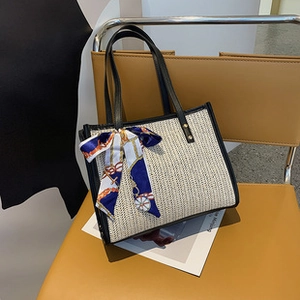Detail of straw woven tote bag with black leather trim and a silk scarf bow on the handle