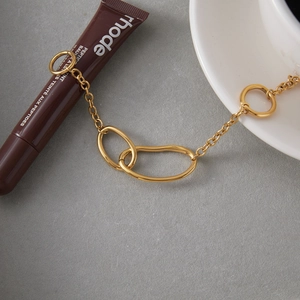 Detail of chunky gold chain bracelet with irregular oval links on a textured background