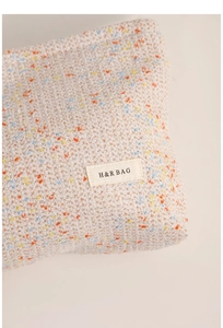 Close-up of beige tweed makeup bag fabric with colorful flecks and H&R BAG logo