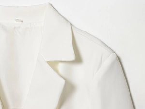 Gros plan détaillé du col du blazer blanc et des coutures sur un tissu tissé lisse