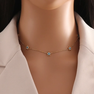 Gold star chain necklace with blue evil eye pendants worn by model over beige blazer