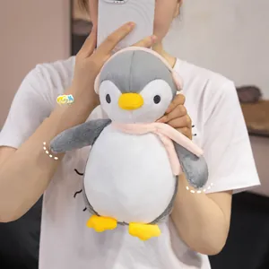 Plush penguin doll featuring pink scarf and earmuffs shown in a lifestyle indoor setting