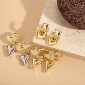 Three pairs of elegant heart pendant hoop earrings displayed on natural stone props