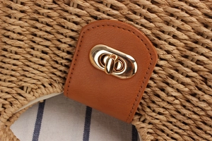 Detail of brown leather buckle with gold metal twist lock on straw woven bag texture