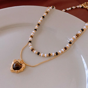 Detail of layered gold necklace featuring a heart-shaped tiger eye stone and beaded chain