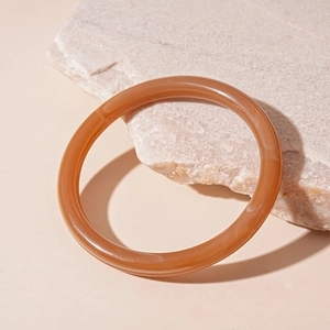 Detail view of a translucent amber resin round bangle on a natural stone surface