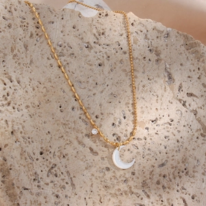 Detail of gold chain necklace with white moon pendant on natural rock texture