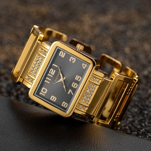 Detail of a luxury gold square watch with a black dial and rhinestone accents on leather